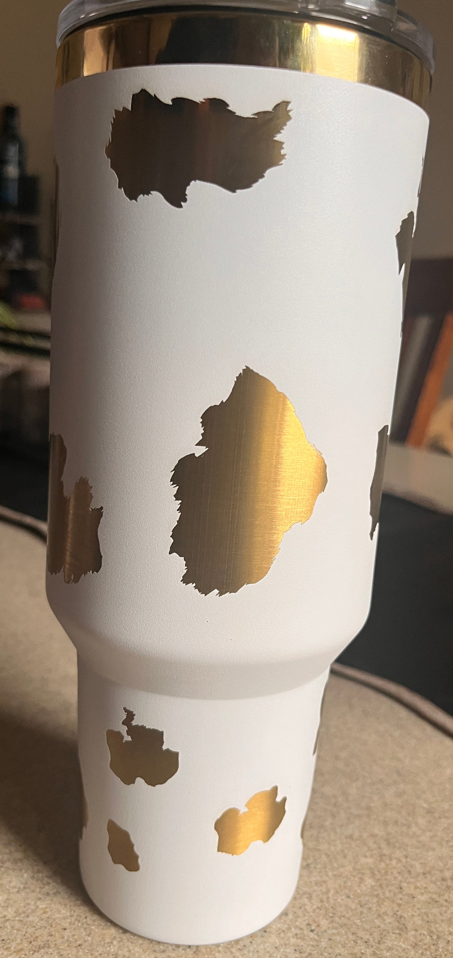 White tumbler with gold cut-out designs on a blurred background